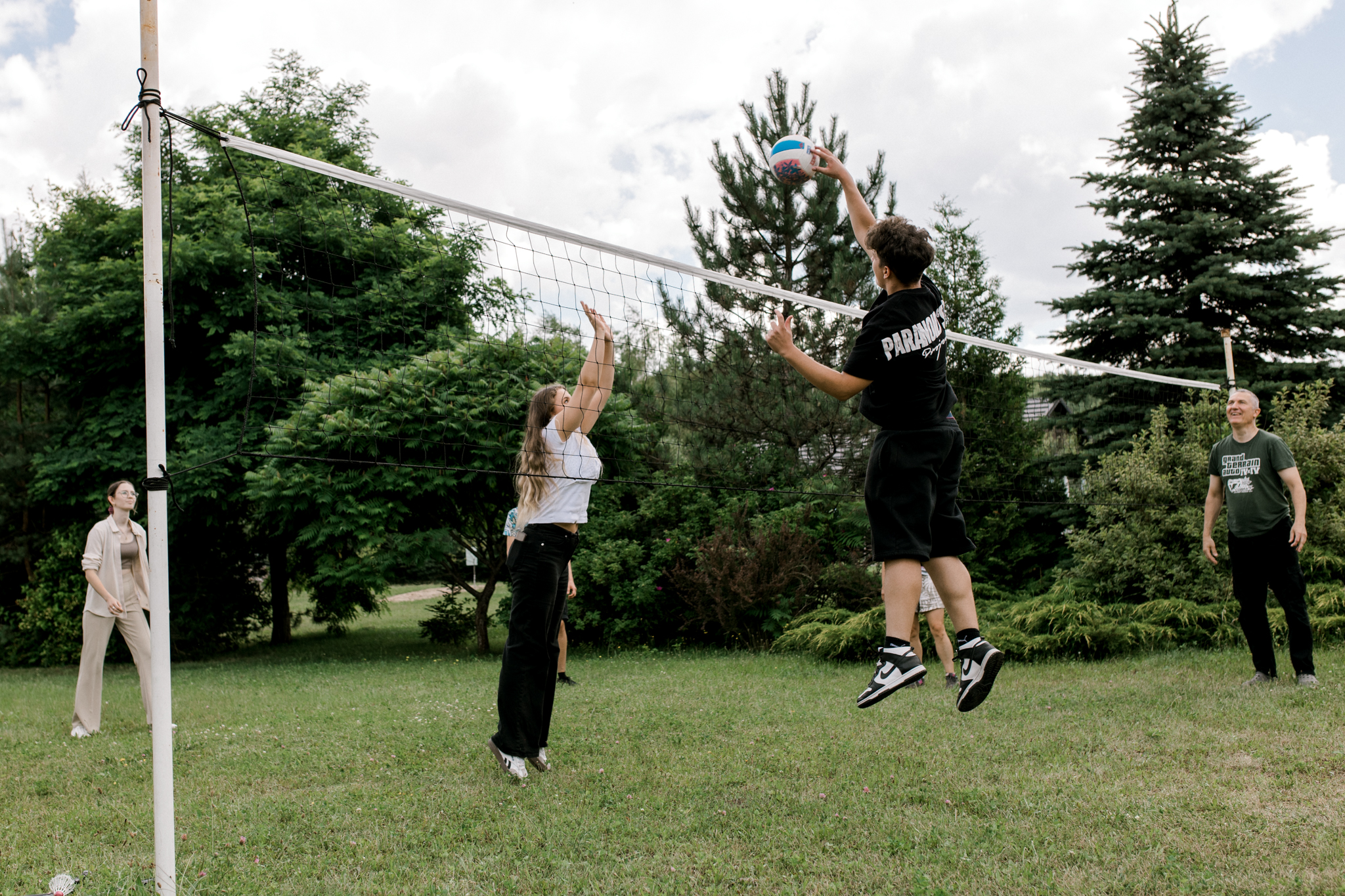 Gracze skaczący do piłki podczas gry w siatkówkę na świeżym powietrzu na trawie z siatką w ogrodzie