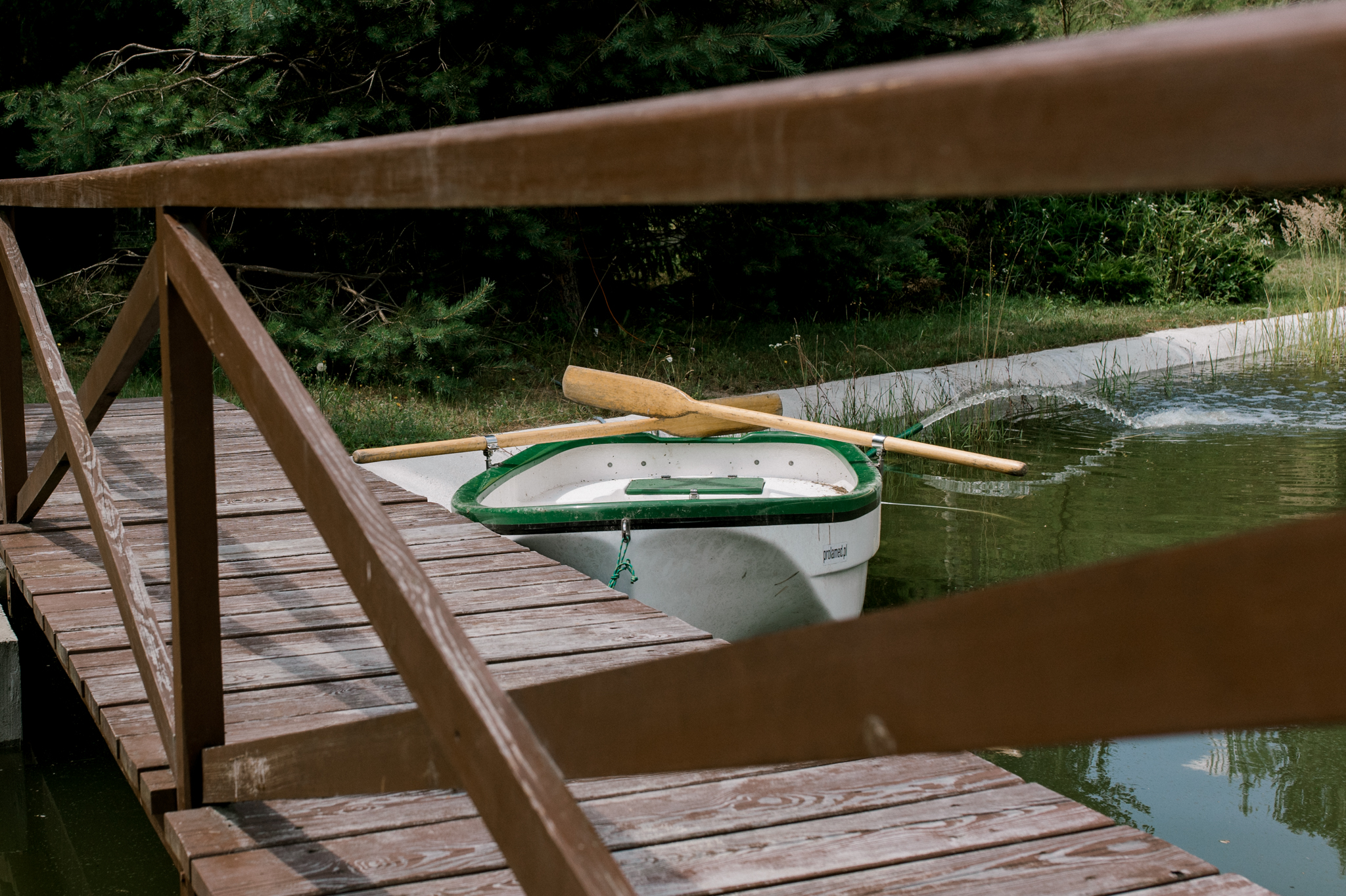 Mała łódka przy drewnianym moście nad stawem, atrakcje wodne w agroturystyce, relaks na wsi Polska