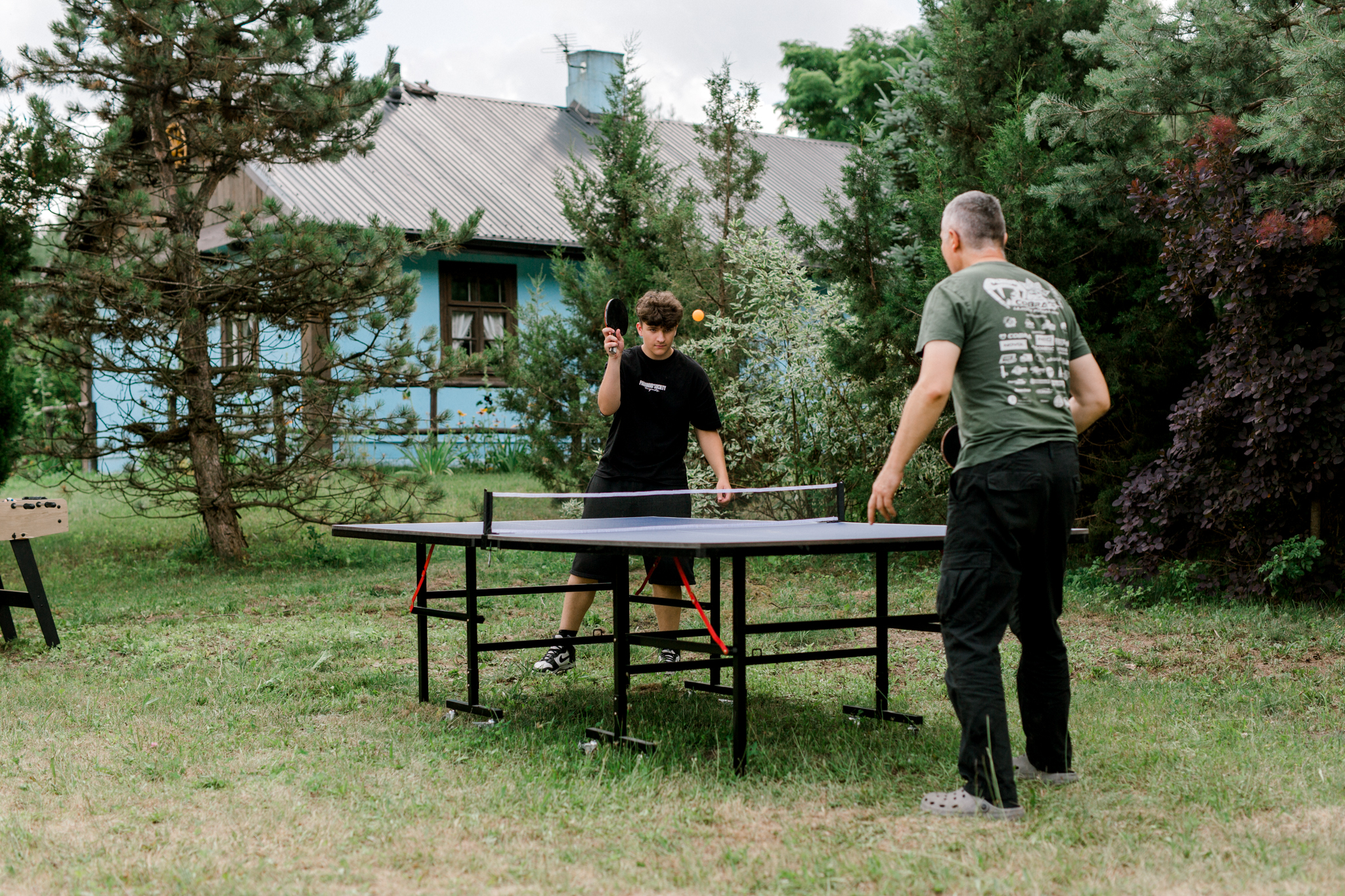 Mężczyźni grający w ping-ponga w ogrodzie przy chacie, sporty rekreacyjne w agroturystyce, wakacje na wsi Polska
