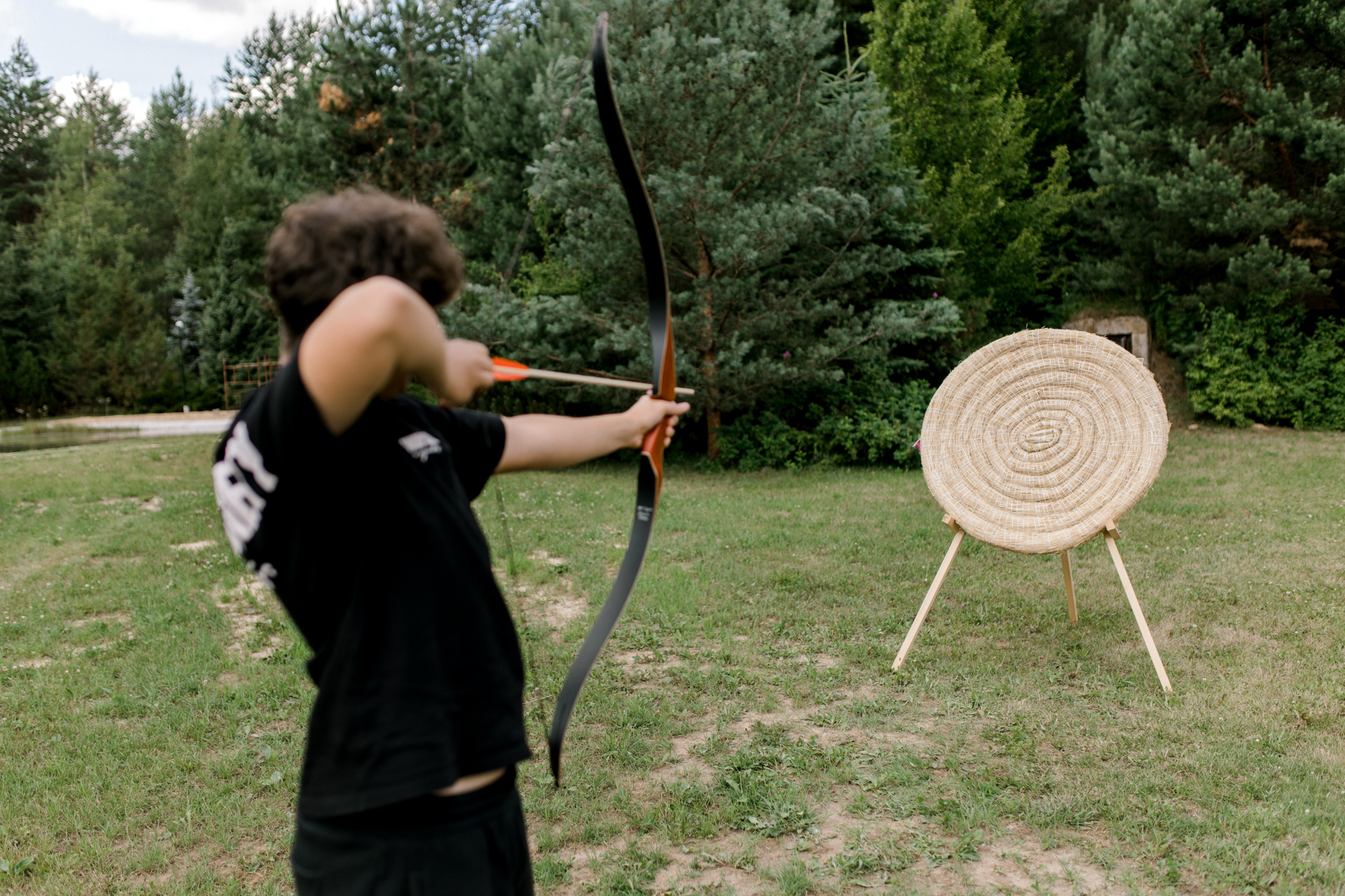 Młody łucznik celujący do tarczy na łące, sporty łucznicze w agroturystyce, atrakcje na świeżym powietrzu Polska
